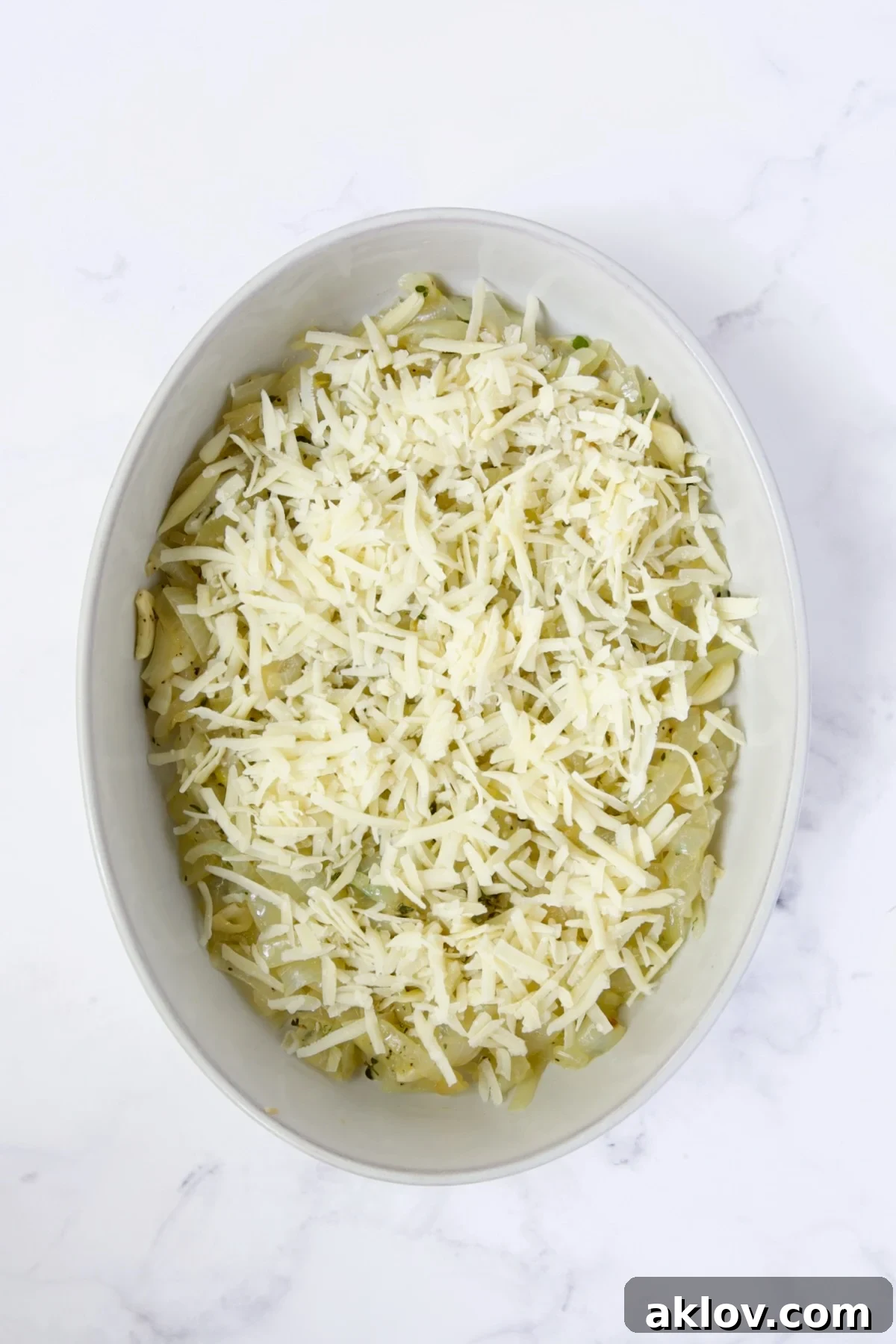 Grated cheese sprinkled over the onion, garlic, and thyme base in the oval baking dish.