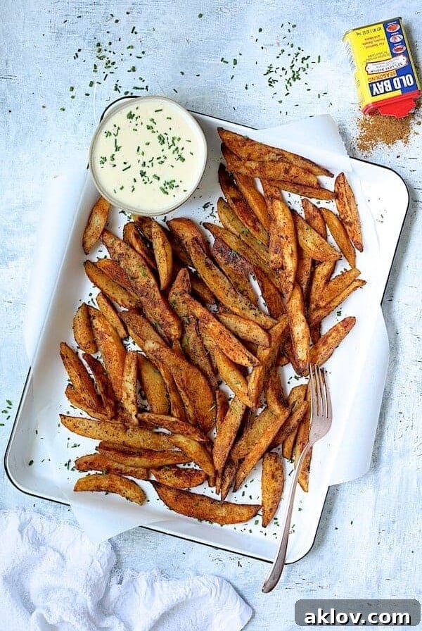 Old Bay Roasted Potato Wedges on white enameled pan with cheese sauce garnished with fresh chives and can of Old Bay.