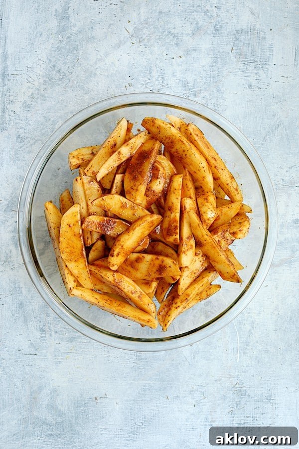 Crunchy Old Bay Wedges, Smothered in Vermont Cheddar 4 Raw potato wedges tossed with oil and vibrant Old Bay Seasoning in a glass mixing bowl, ready for roasting.