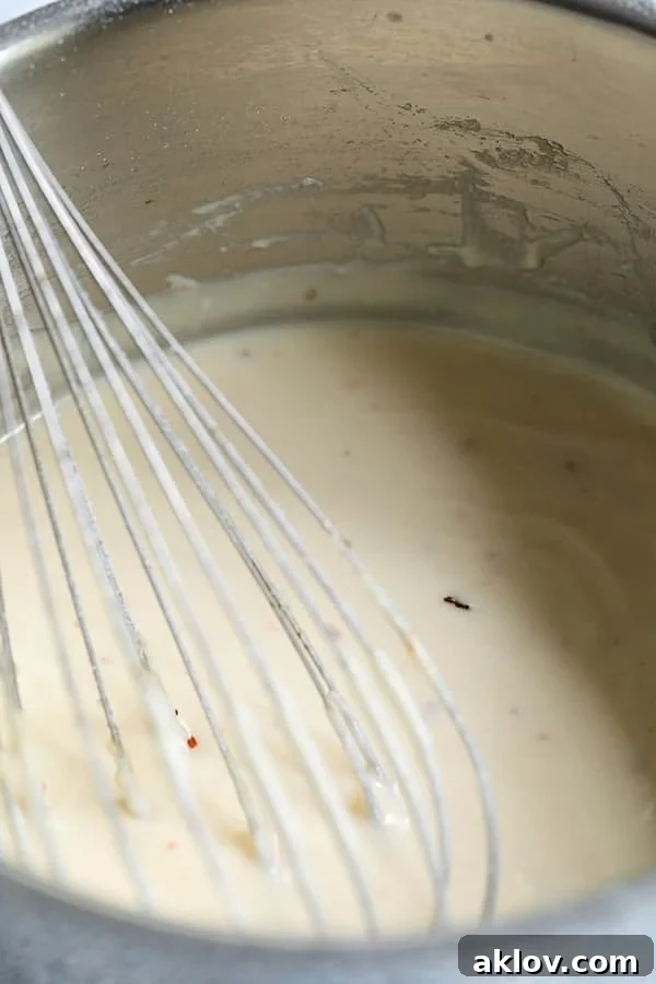 Crunchy Old Bay Wedges, Smothered in Vermont Cheddar 8 A close-up shot of a creamy, golden cheese sauce being vigorously whisked in a silver saucepan, ensuring a smooth, lump-free texture.