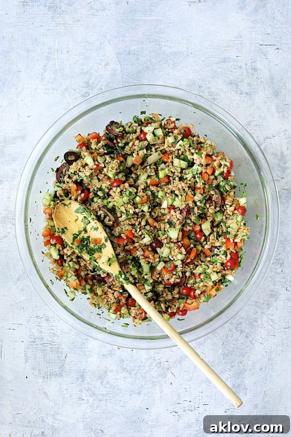 Mediterranean Farro Salad mixed in a large glass mixing bowl with a white serving spoon.