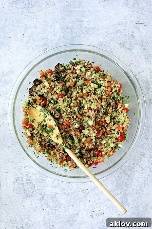 Sun-Drenched Farro Salad 5 The Mediterranean Farro Salad, freshly mixed and tossed with dressing in a clear glass mixing bowl, with a white serving spoon.