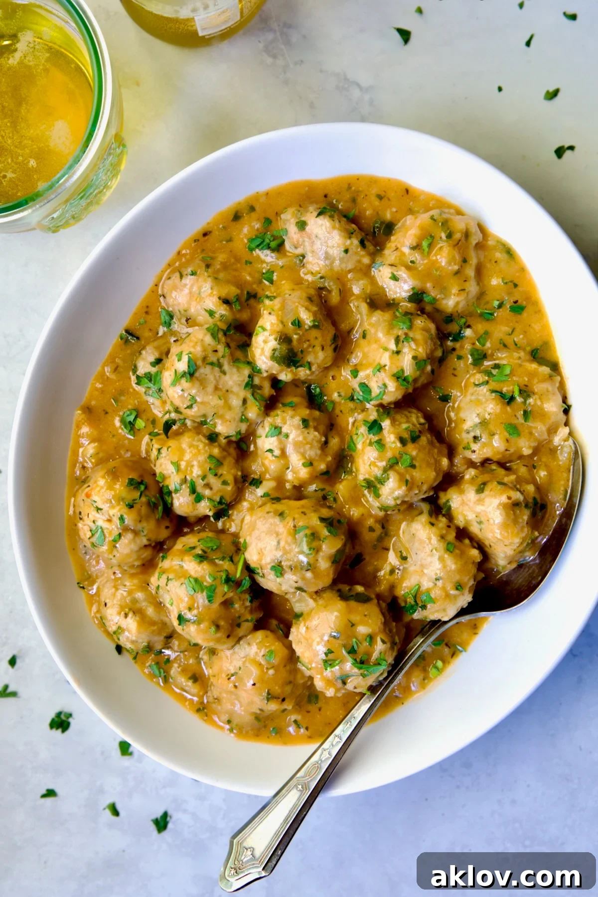 Golden Turkey Meatballs with Ale Glaze 2 Baked Turkey Meatballs in Beer - Onion Sauce in white oval bowl with serving spoon garnished with fresh parsley.