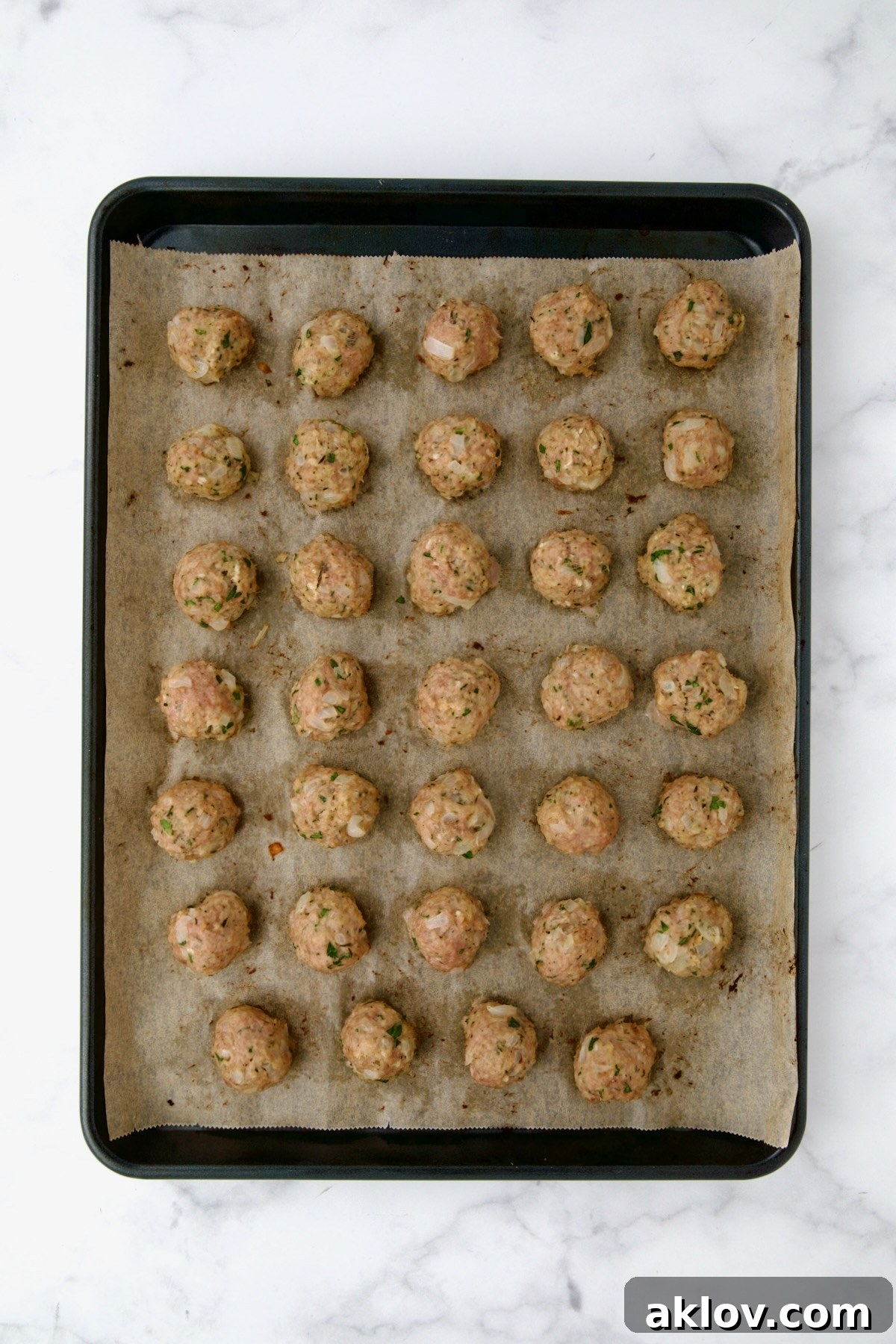 Golden Turkey Meatballs with Ale Glaze 11 34 turkey meatballs on parchment paper on rimmed sheet pan after being baked.