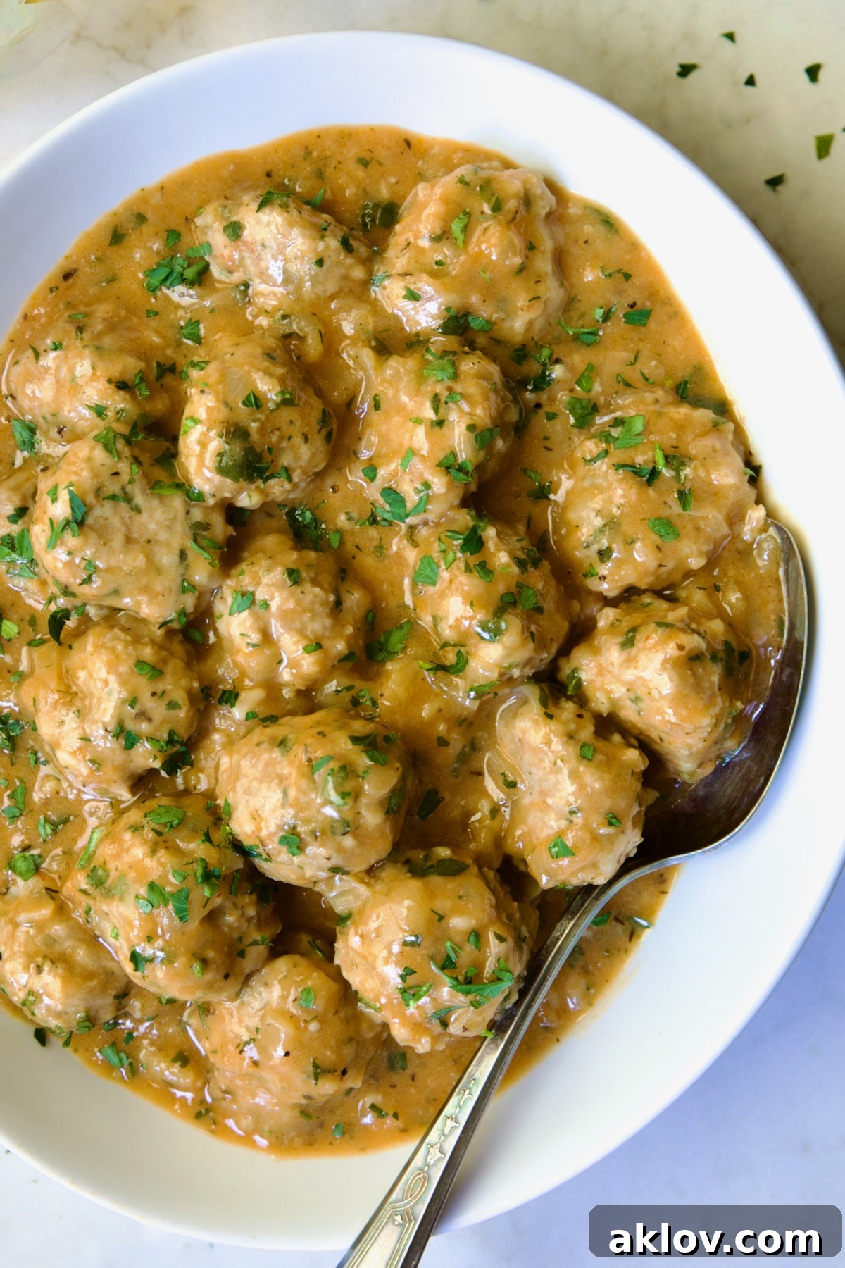 Golden Turkey Meatballs with Ale Glaze 18 Baked Turkey Meatballs in Beer - Onion Sauce in white oval bowl with serving spoon garnished with fresh parsley.