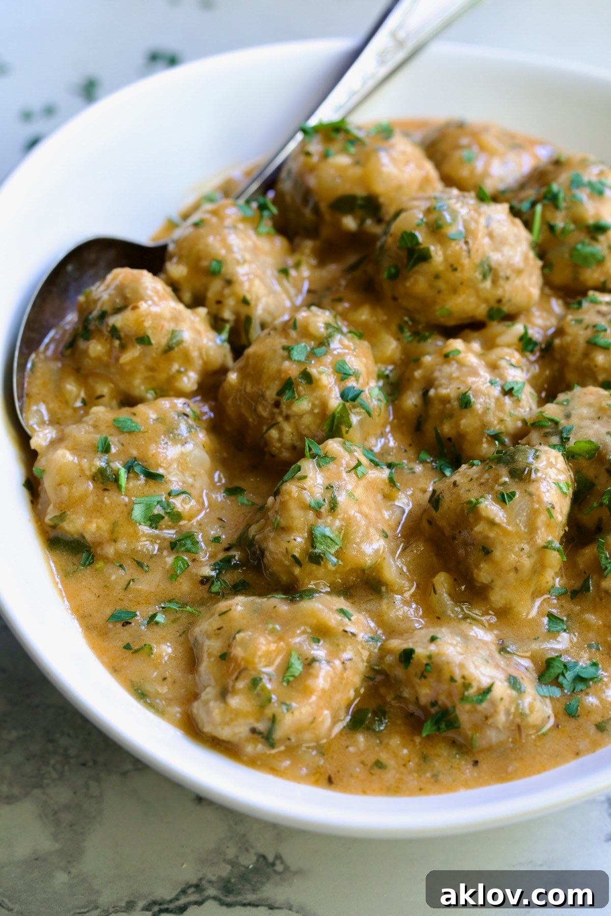 Golden Turkey Meatballs with Ale Glaze 19 Baked Turkey Meatballs in Beer - Onion Sauce in white oval bowl with serving spoon garnished with fresh parsley.