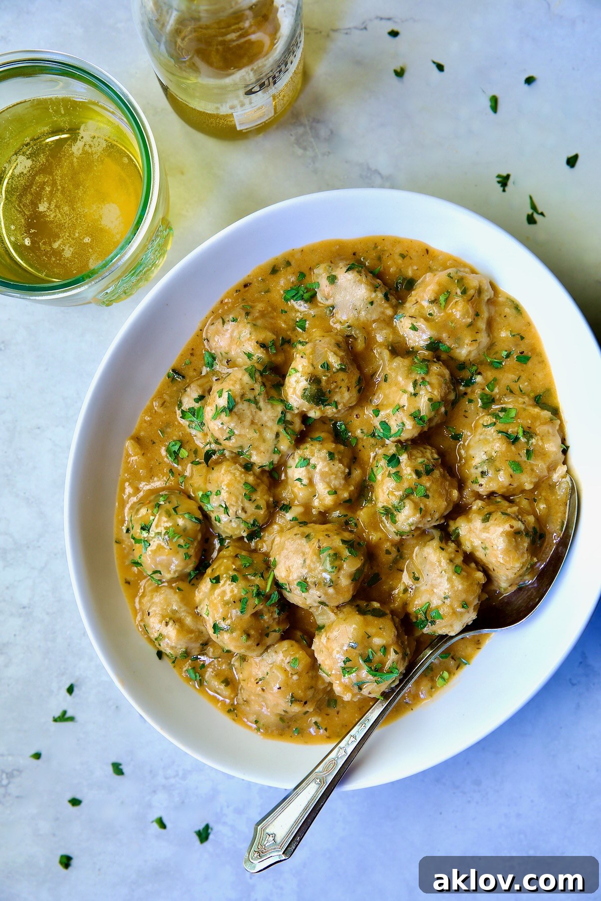 Golden Turkey Meatballs with Ale Glaze 20 Baked Turkey Meatballs in Beer - Onion Sauce in white oval bowl with serving spoon garnished with fresh parsley.