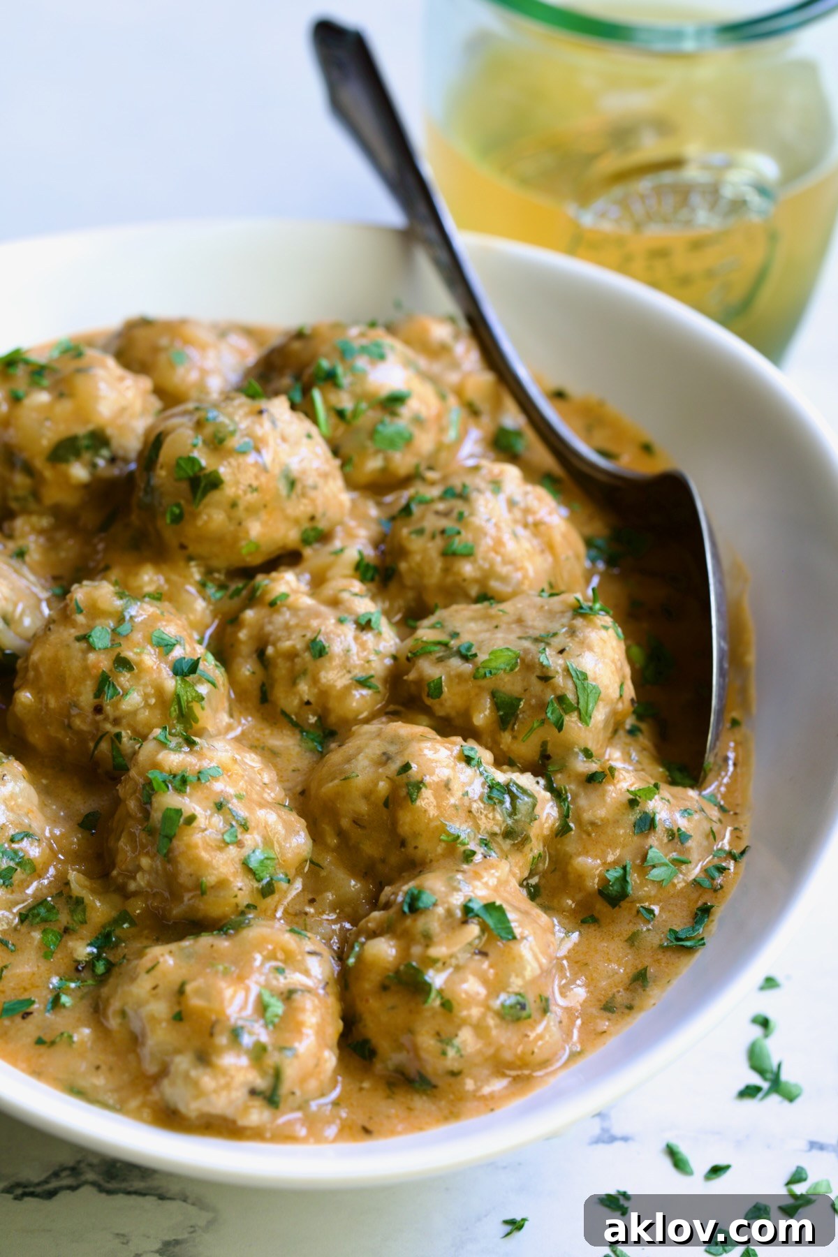 Golden Turkey Meatballs with Ale Glaze 3 Baked Turkey Meatballs in Beer - Onion Sauce in white oval bowl with serving spoon garnished with fresh parsley.
