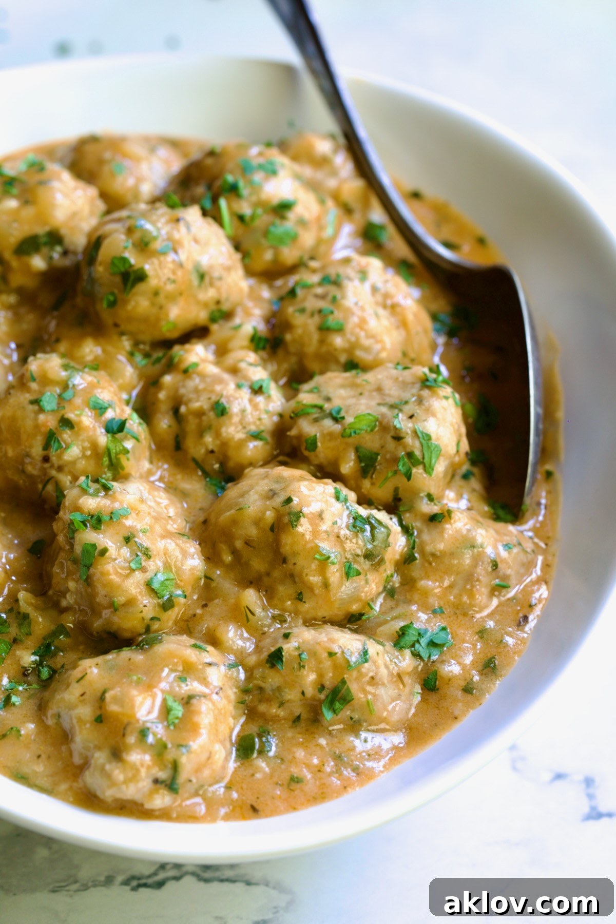 Golden Turkey Meatballs with Ale Glaze 21 Baked Turkey Meatballs in Beer - Onion Sauce in white oval bowl with serving spoon garnished with fresh parsley.