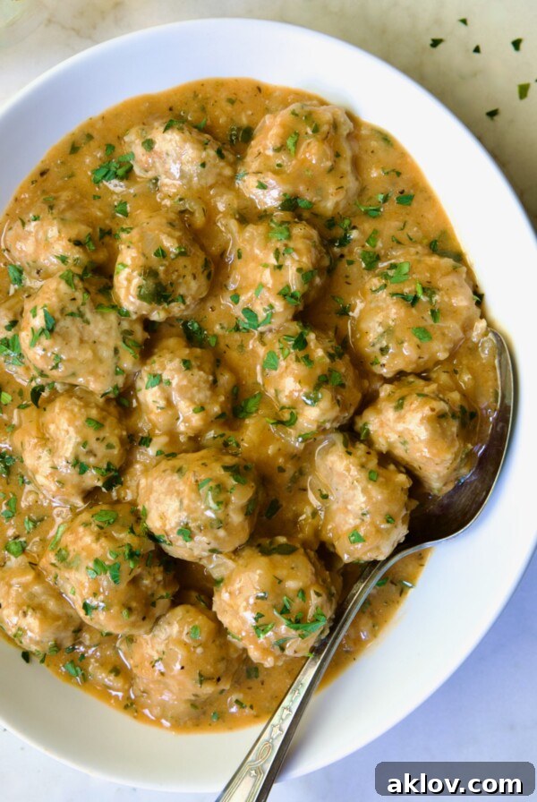 Golden Turkey Meatballs with Ale Glaze 22 Baked Turkey Meatballs in Beer - Onion Sauce in white oval bowl with serving spoon garnished with fresh parsley.
