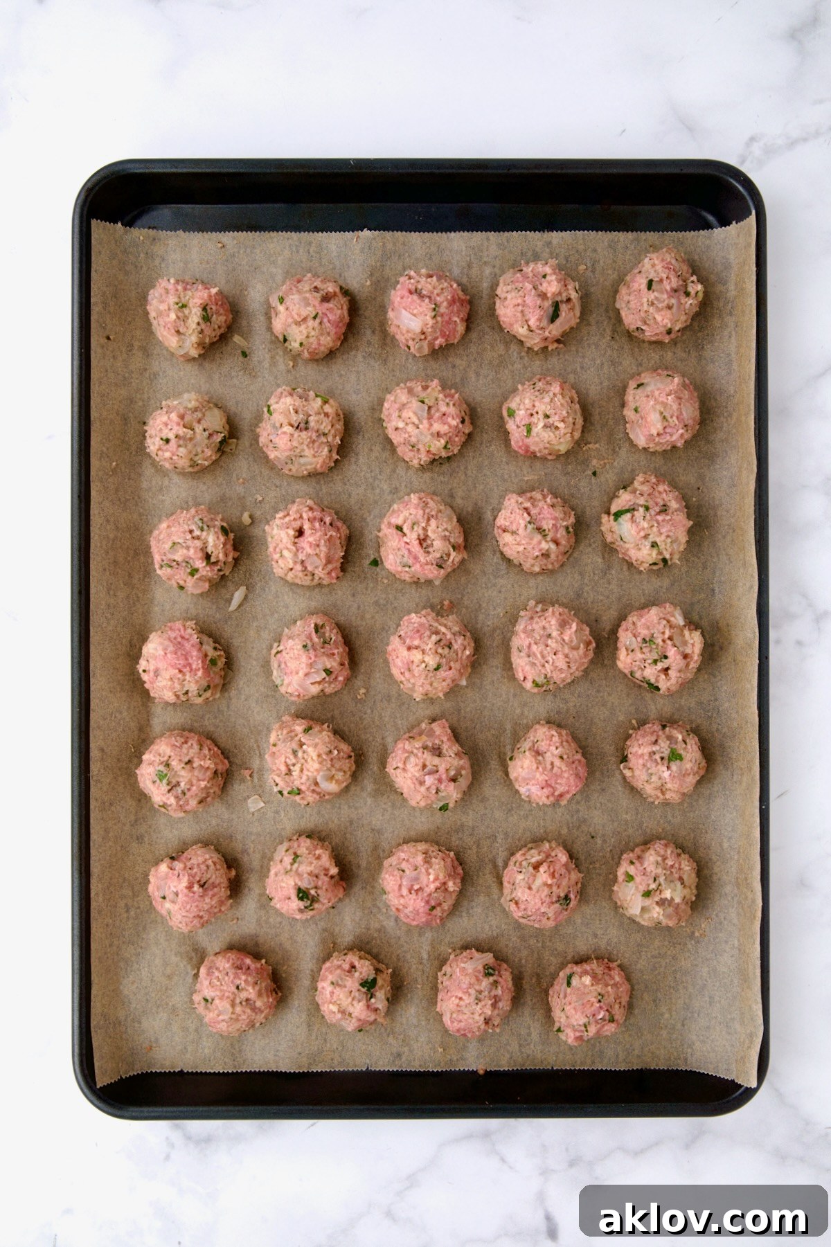 Golden Turkey Meatballs with Ale Glaze 10 34 turkey meatballs on parchment paper on rimmed sheet pan before being baked.