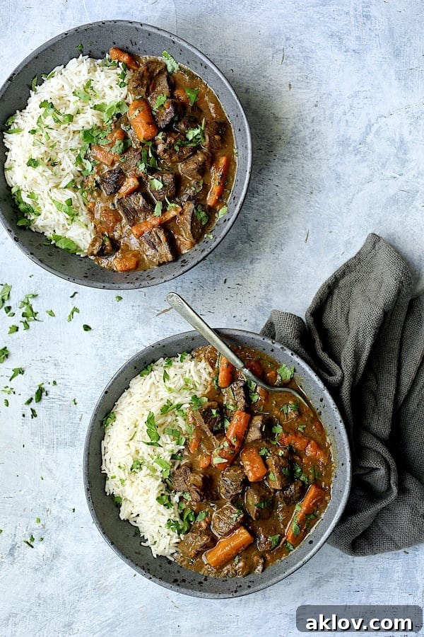 Two servings of rich Pressure Cooker Indian Curry Beef Stew with fluffy white basmati rice, presented in gray bowls on a pale blue background with a dark gray napkin.