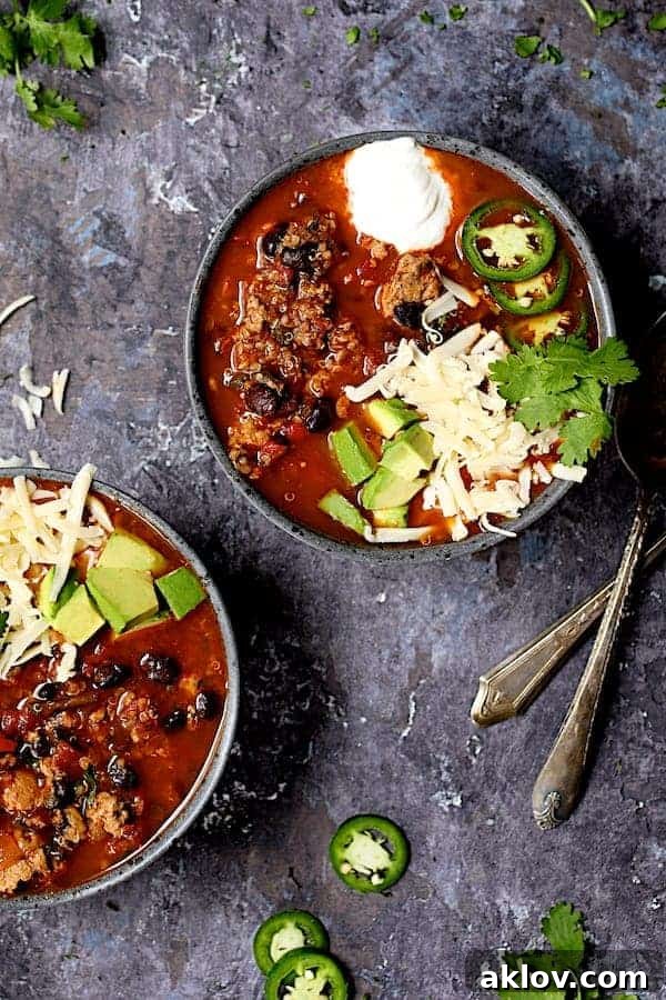 Overhead shot of Turkey Black Bean Quinoa Chili garnished with fresh avocado, sliced jalapeno, shredded cheese, and a dollop of sour cream, served in a rustic gray bowl.