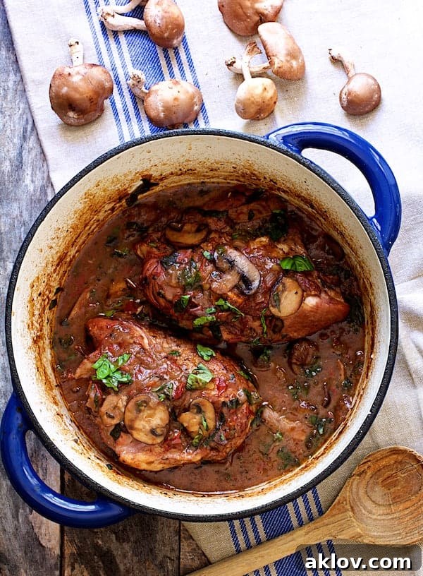 Photo of Chicken Pinot Noir with Wild Mushrooms and Fresh Basil in blue Dutch oven on blue-striped towel.