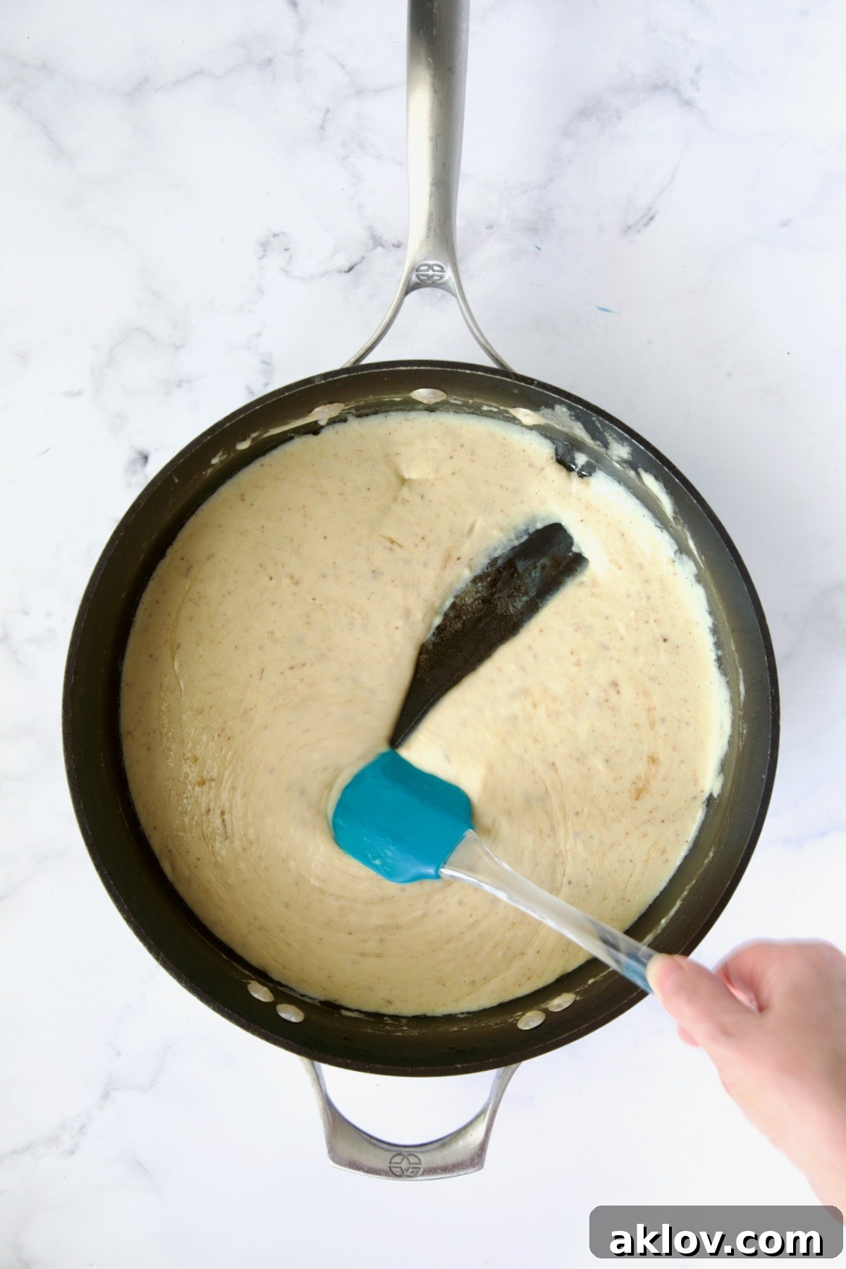 Cheese sauce in nonstick skillet with blue spatula.