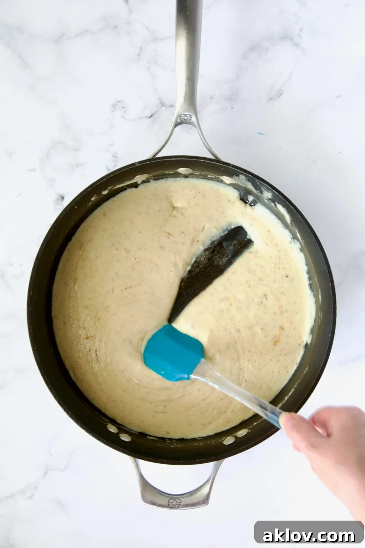 The fully incorporated, smooth cheese sauce gleaming in a nonstick skillet, ready for the next steps, with a blue spatula.