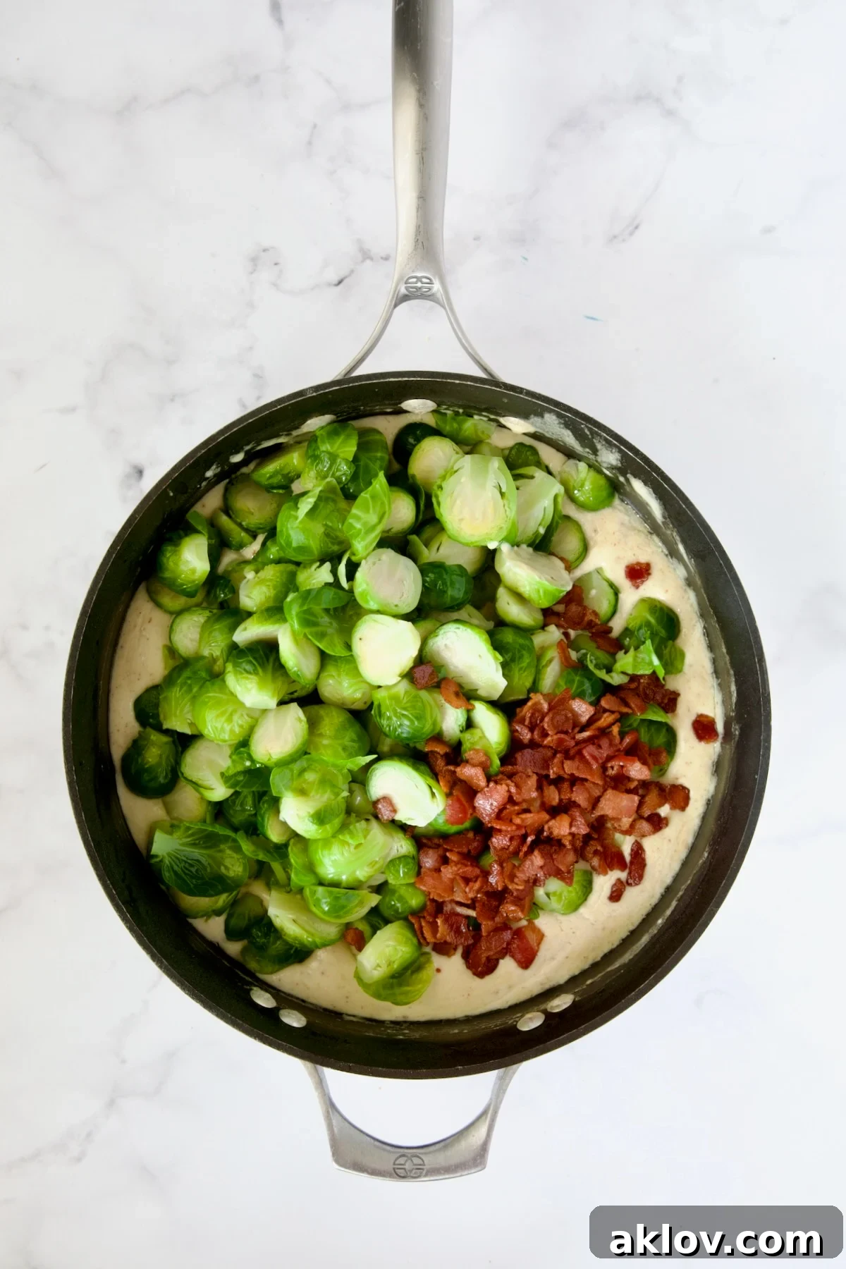 Blanched Brussels sprouts and crispy bacon being added to the rich cheese sauce in a nonstick skillet.