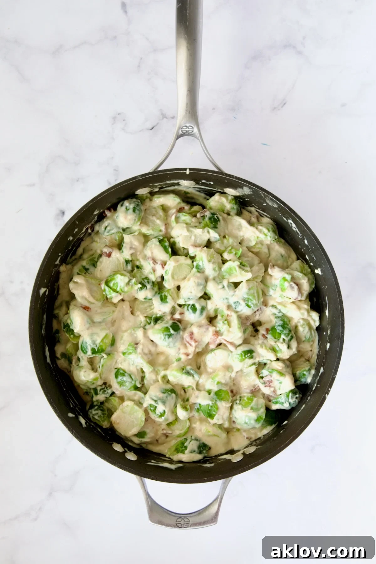 Blanched Brussels sprouts and bacon fully combined with the creamy cheese sauce in a nonstick skillet, ready for assembly.