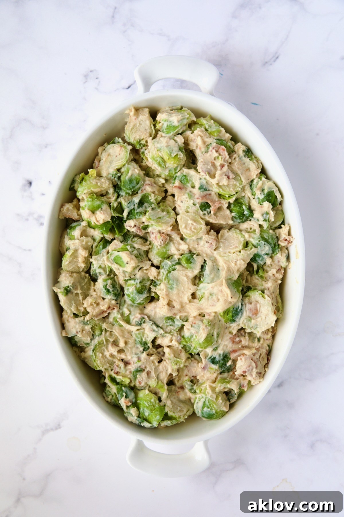 Brussels sprouts in cheese sauce are transferred to an oval baking dish.