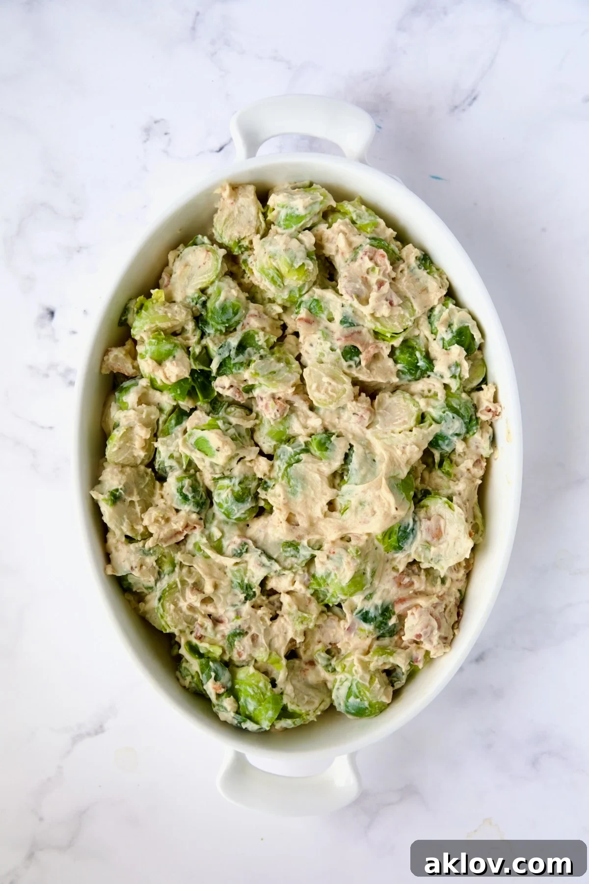 The delicious Brussels sprouts in cheese sauce carefully transferred to an oval baking dish, preparing for the topping.