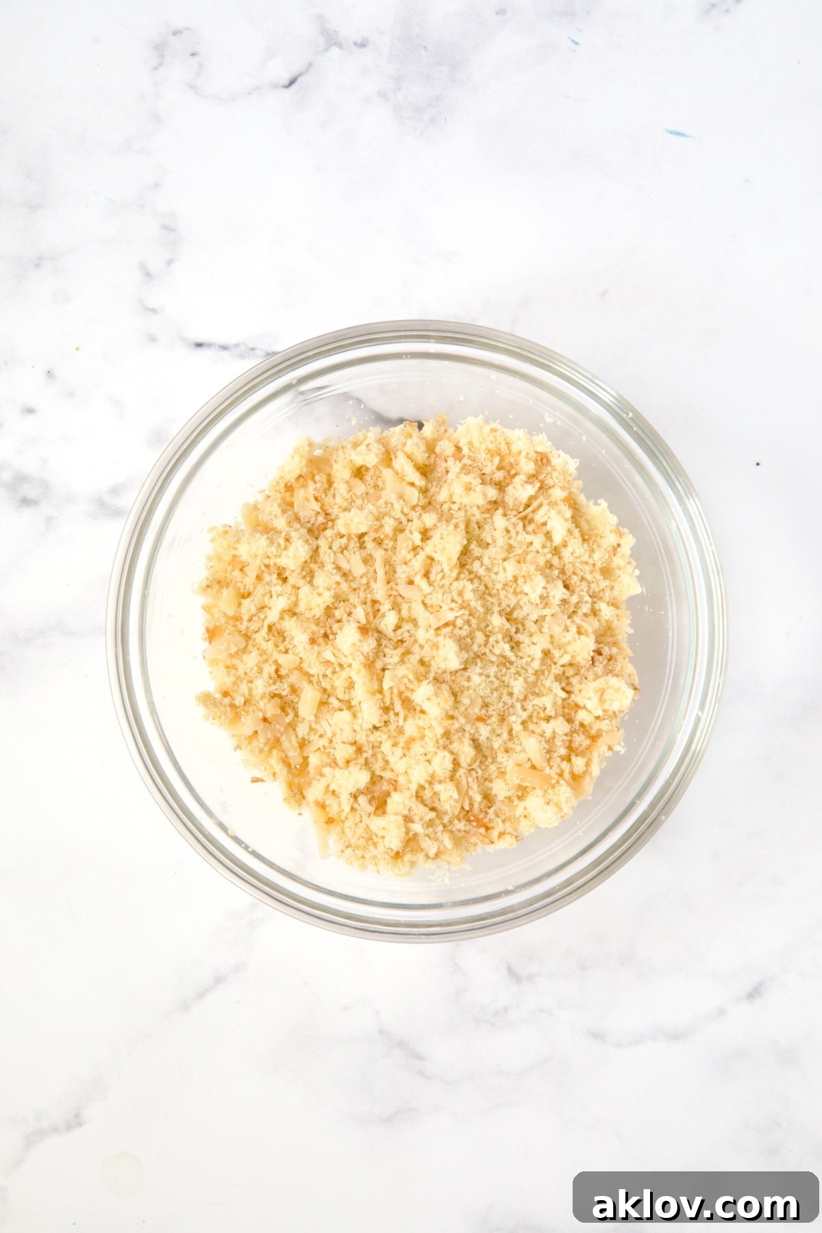 Breadcrumbs, cheese and butter mixed together in glass bowl.