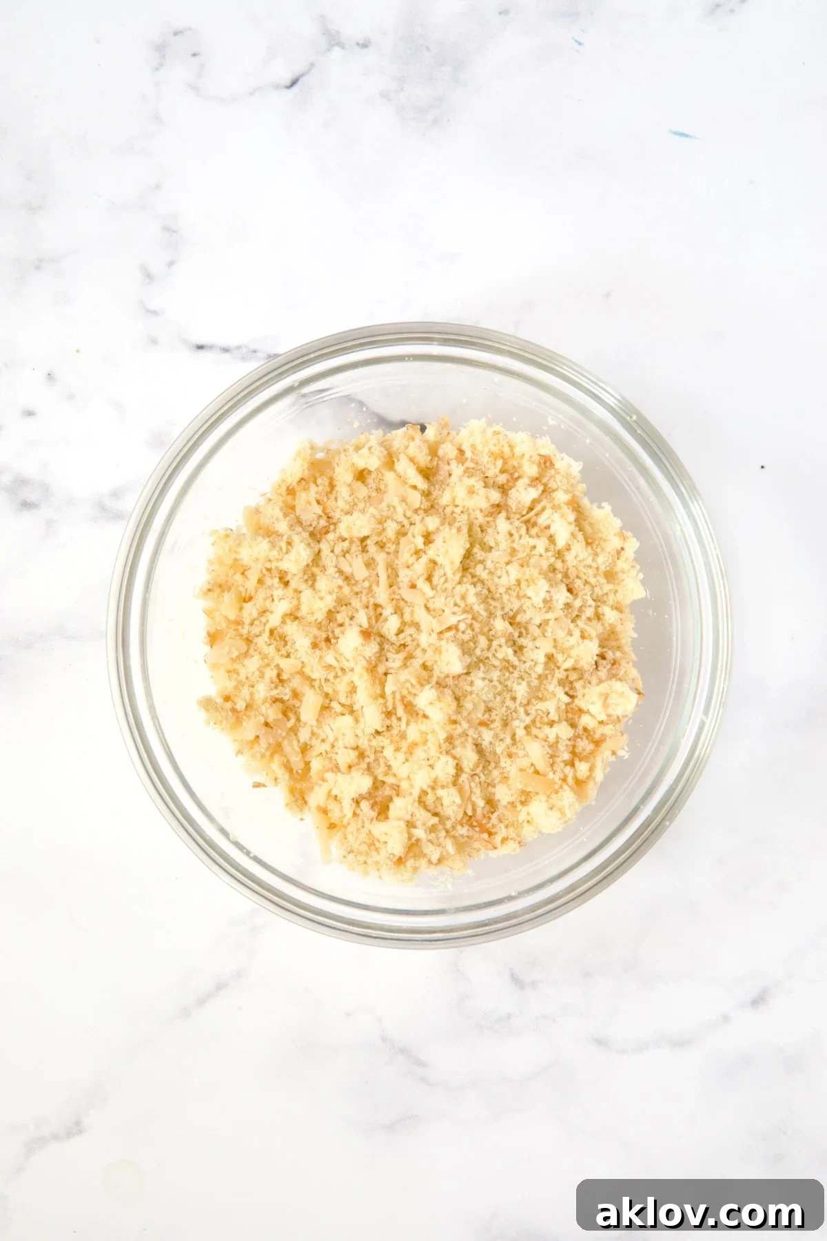 A small glass bowl holding a perfectly mixed blend of breadcrumbs, grated Parmesan cheese, and softened butter.