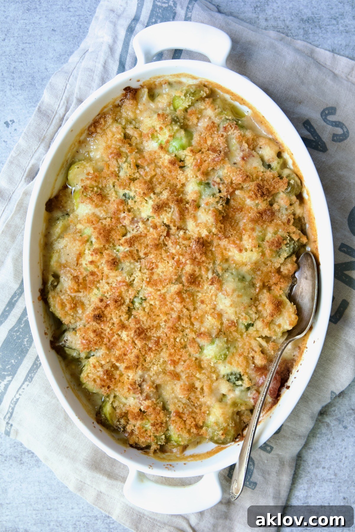 Fully baked Brussels Sprouts Gratin on a blue striped towel with a serving spoon.
