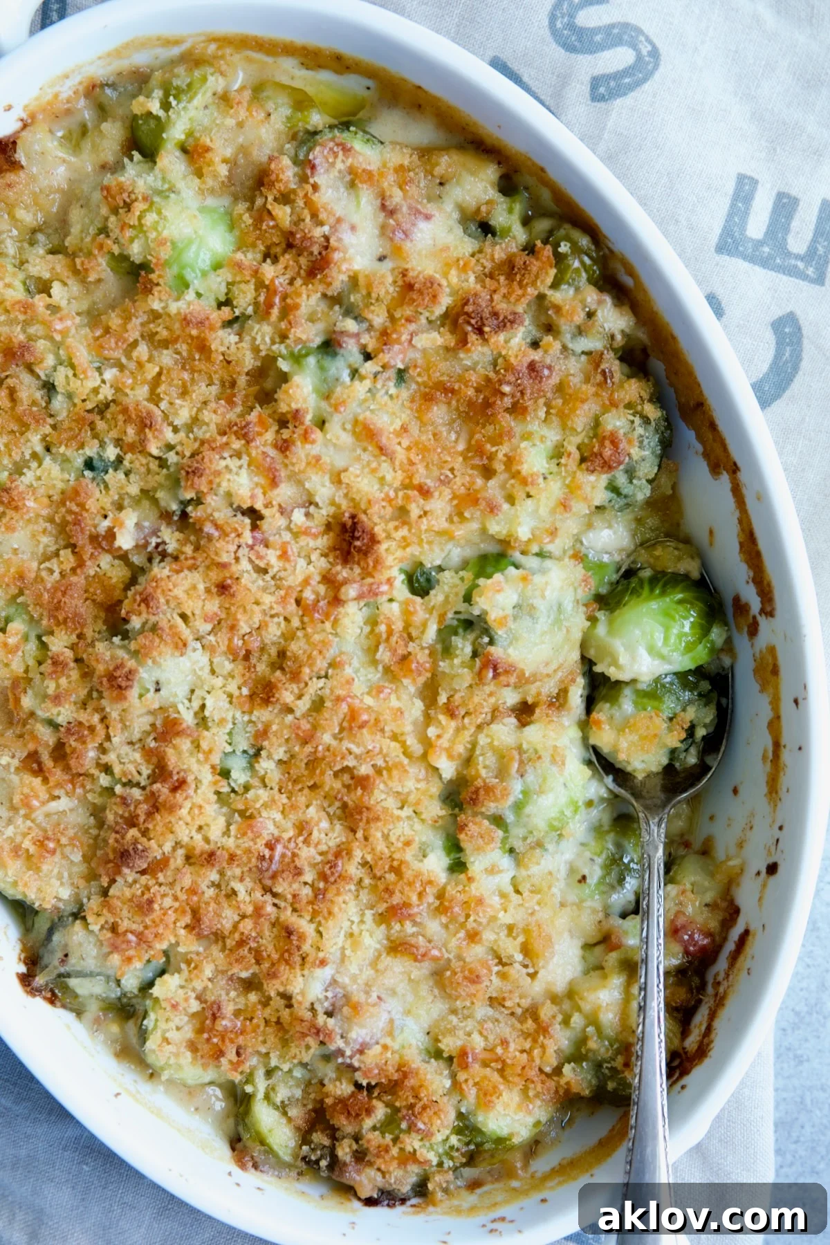 A delicious serving of Brussels Sprouts Gratin in an oval baking dish, with a spoon ready to serve.