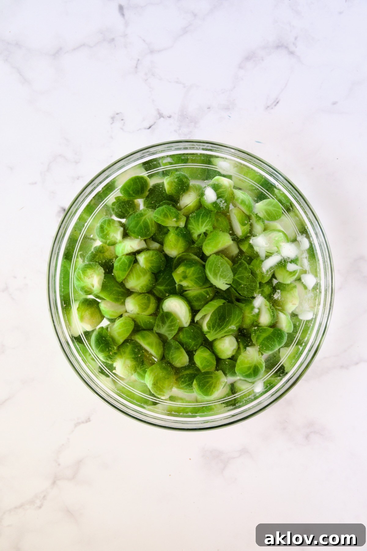 Blanched Brussels sprouts halves in ice bath in glass bowl.