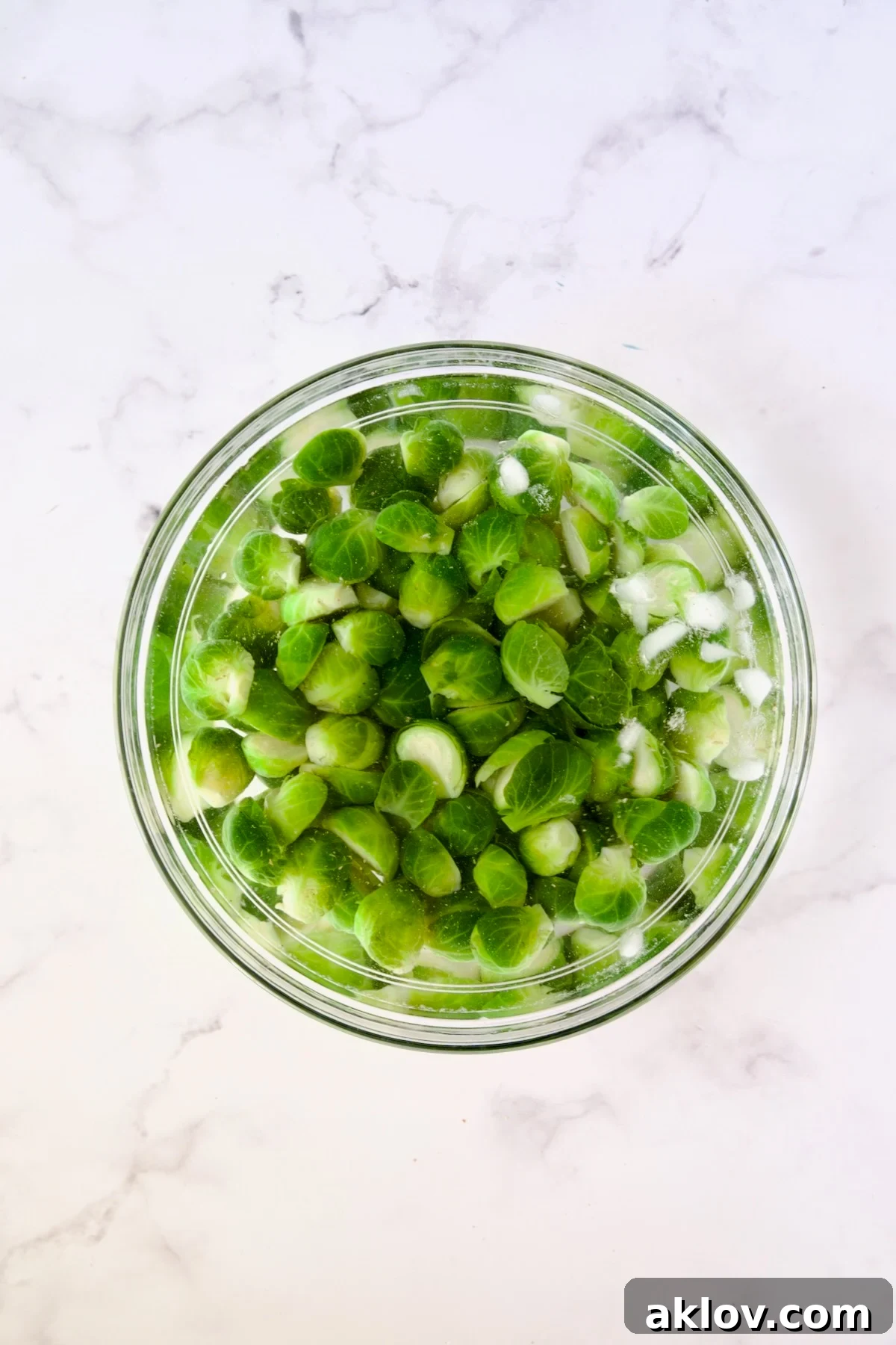 Blanched Brussels sprouts halves submerged in an invigorating ice bath within a clear glass bowl.