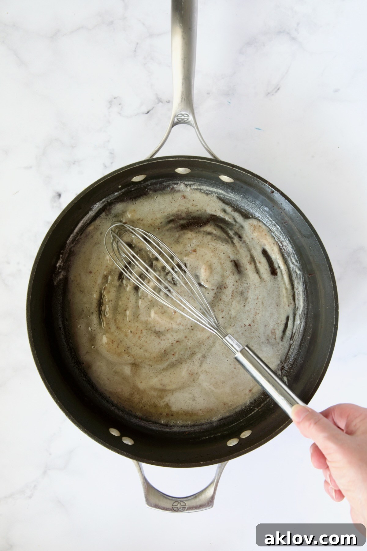 Flour being whisked into bacon drippings in nonstick skillet.
