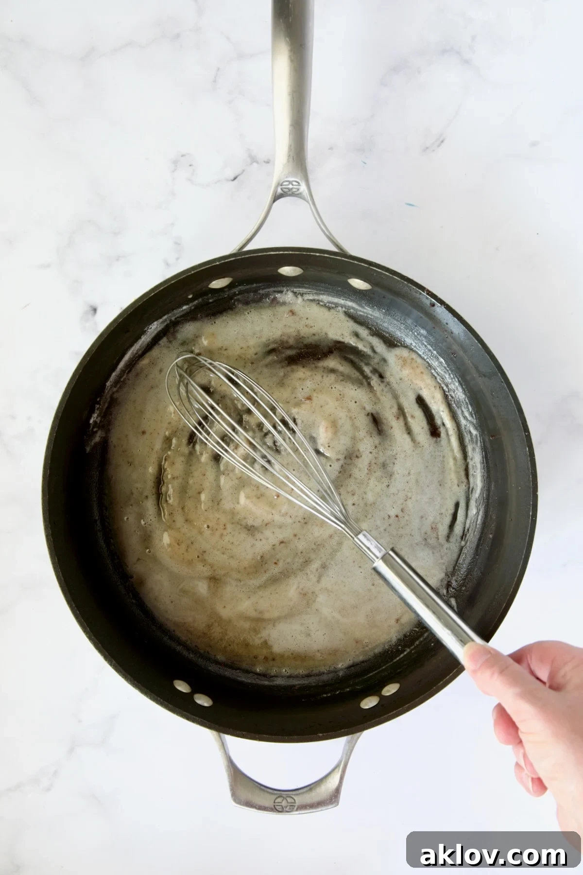 All-purpose flour being expertly whisked into the flavorful bacon drippings in a nonstick skillet, forming a roux.
