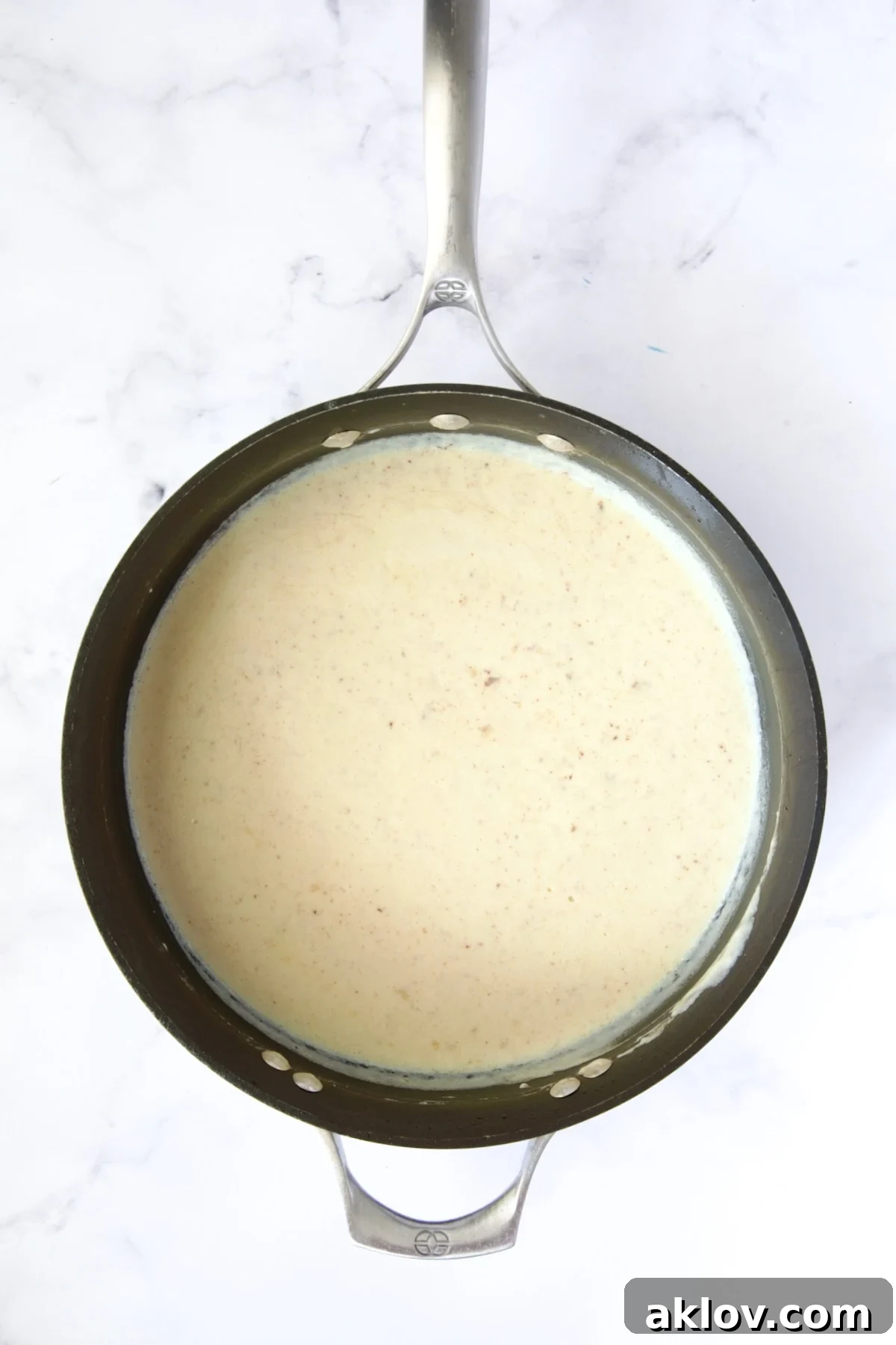 A rich, creamy white sauce gently simmering in a nonstick skillet, forming the luxurious base for the gratin.