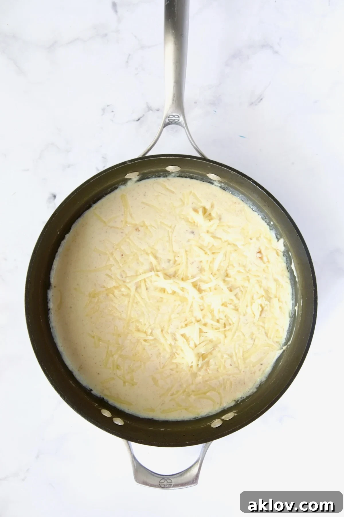 Shredded cheese gradually melting into the velvety cream sauce in a nonstick skillet, creating a smooth consistency.