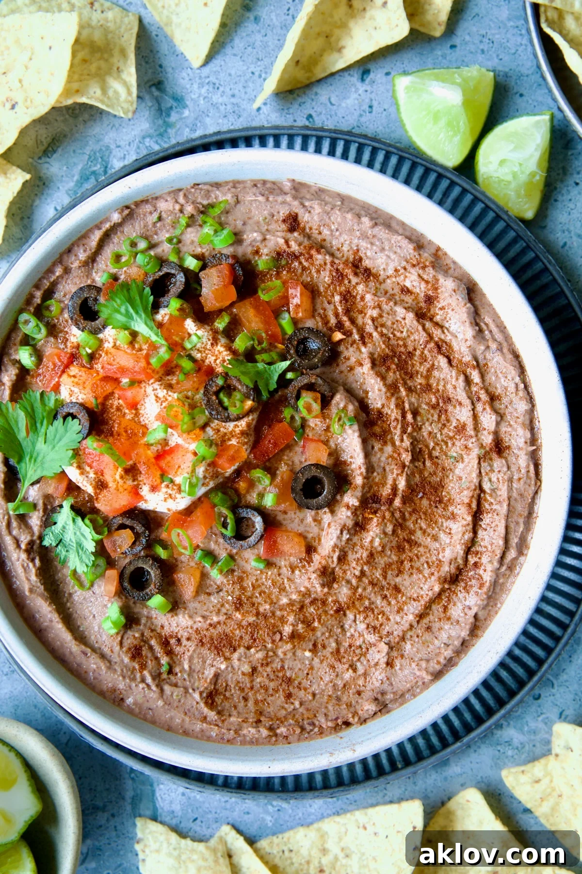 Zesty Black Bean Delight 2 Creamy Black Bean Dip in a white clay bowl, surrounded by crispy tortilla chips and fresh lime wedges, ready for serving.