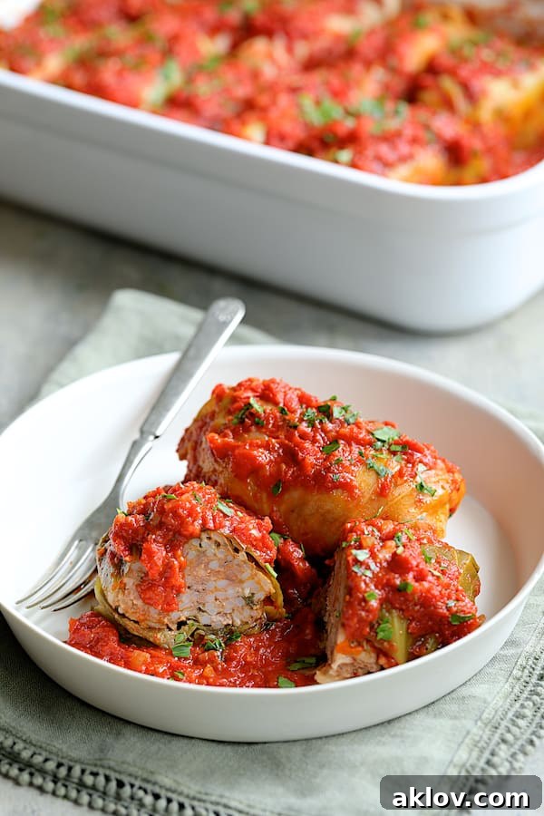 Two spicy Italian stuffed cabbage rolls in a white bowl, one cut in half to showcase the delicious meat and rice filling.