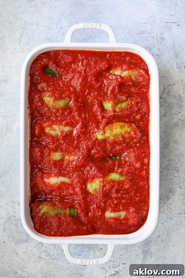 Overhead shot of sauced stuffed cabbage rolls, nestled in the baking dish and glistening, ready to be baked to perfection.