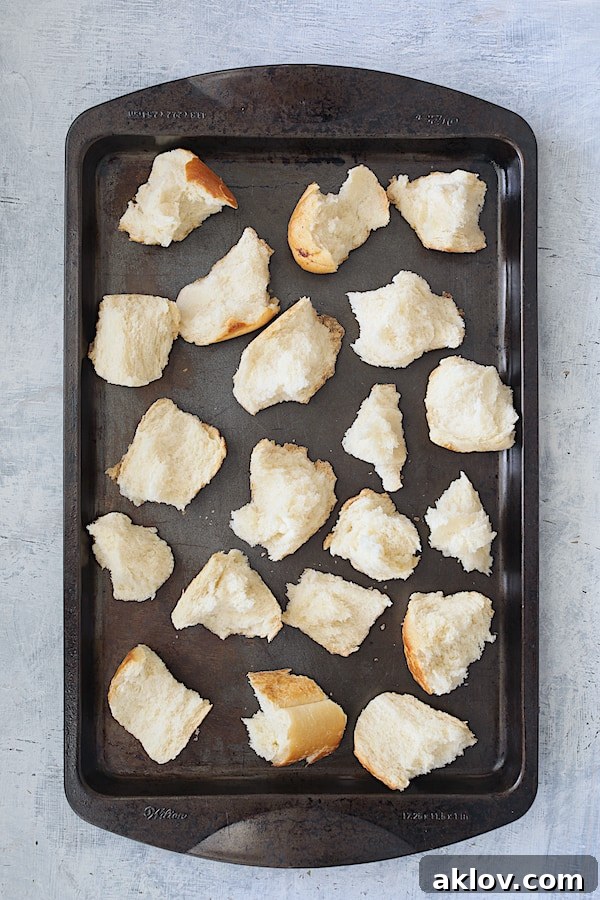 Overhead shot of unbaked torn sourdough croutons on a baking sheet, drizzled with oil and seasonings.