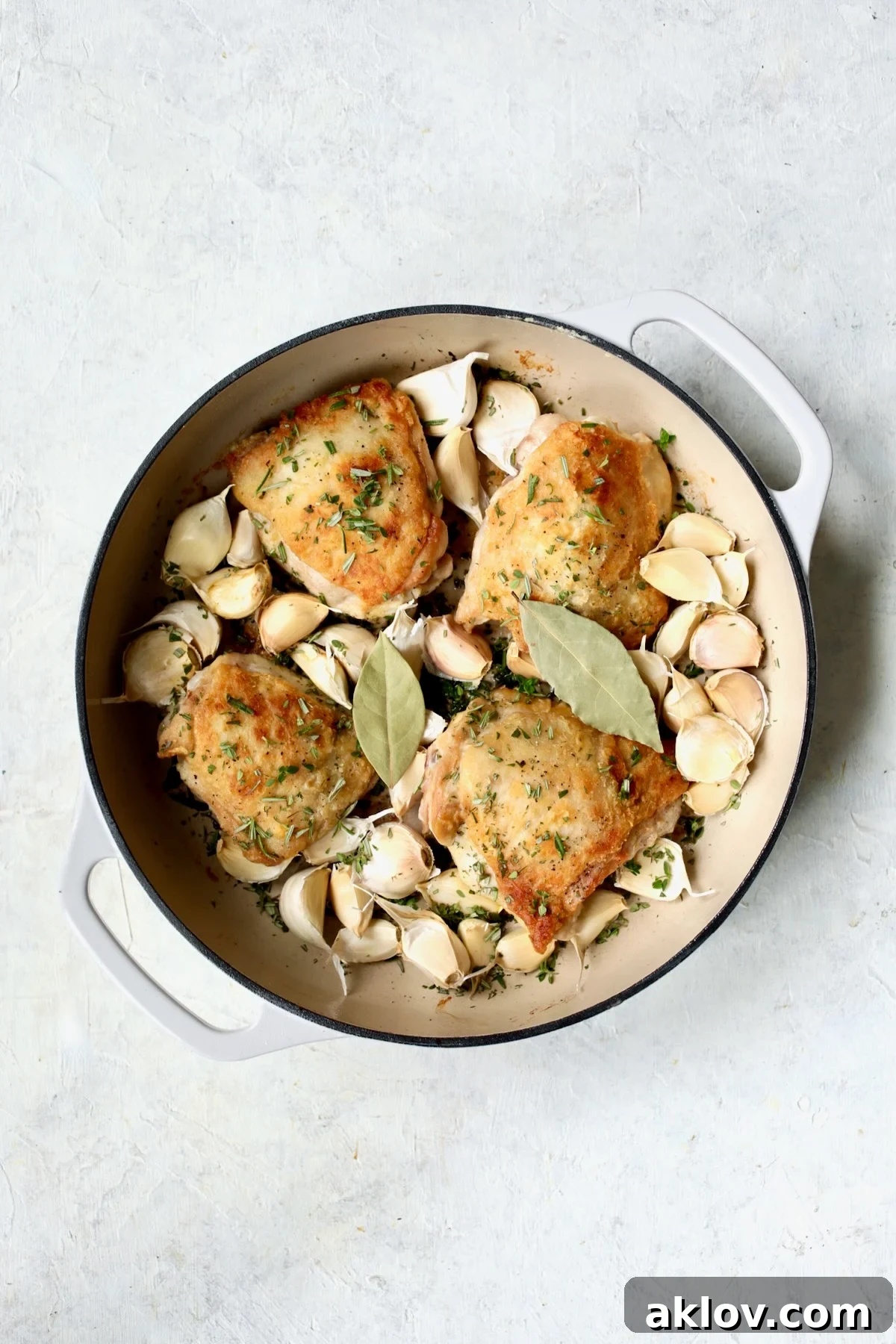 Unpeeled garlic cloves added to browned chicken thighs in white enamel cast iron skillet.