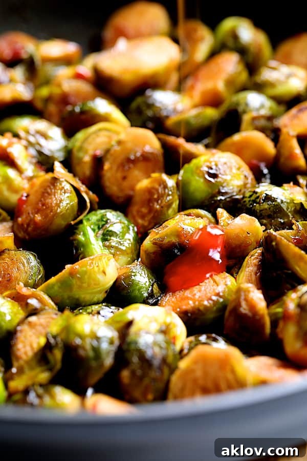 Photo of Brussels sprouts in skillet with sweet chili sauce being drizzled on.