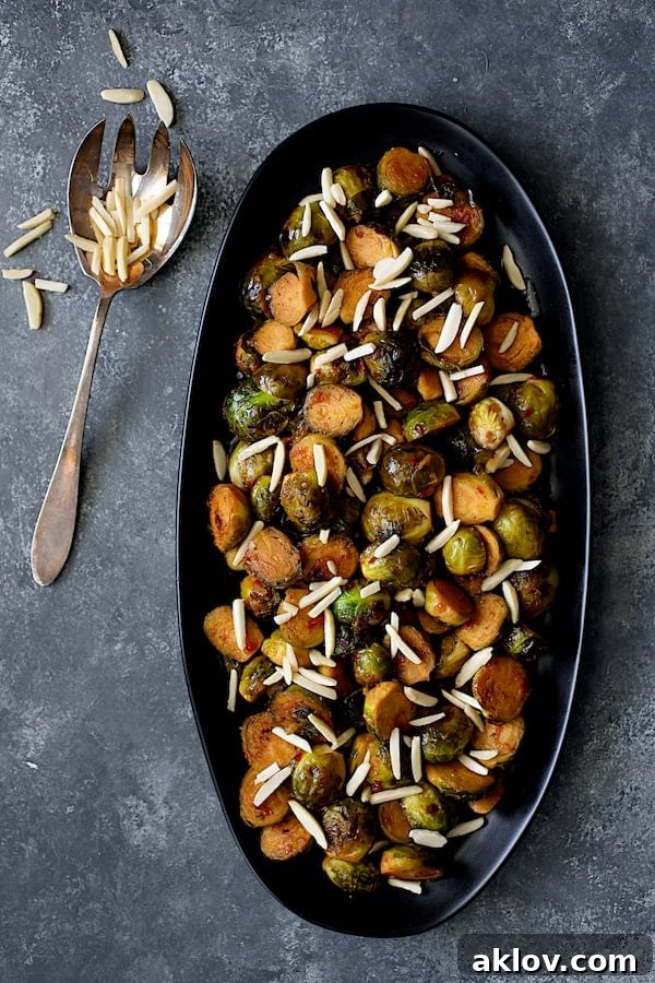 Photo of Pan-Roasted Brussels Sprouts with Thai Sweet Chili Orange Glaze on black serving platter with almonds scattered over.