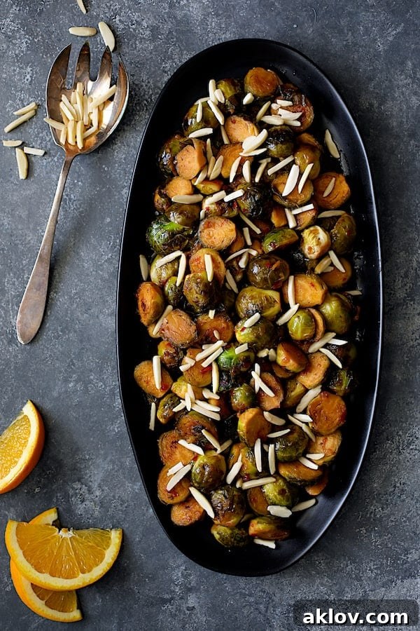 Photo of Pan-Roasted Brussels Sprouts with Thai Sweet Chili Orange Glaze on black platter with orange wedges.