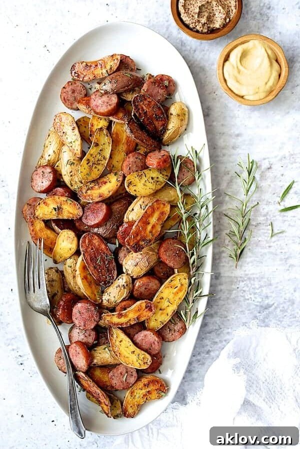 Duck Fat Roasted Fingerlings with Sausage on oval white platter garnished with fresh rosemary.
