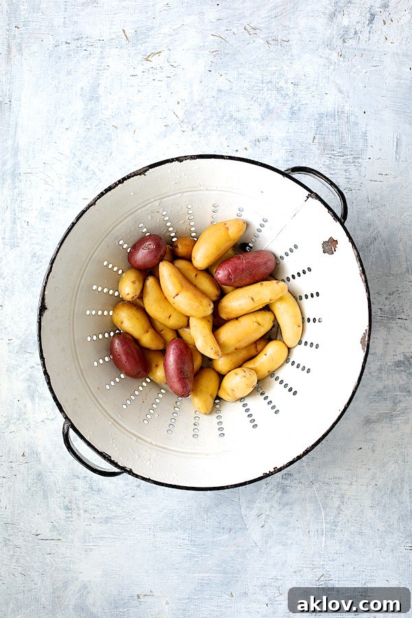 A vintage white colander filled with washed and halved fingerling potatoes, ready for roasting.