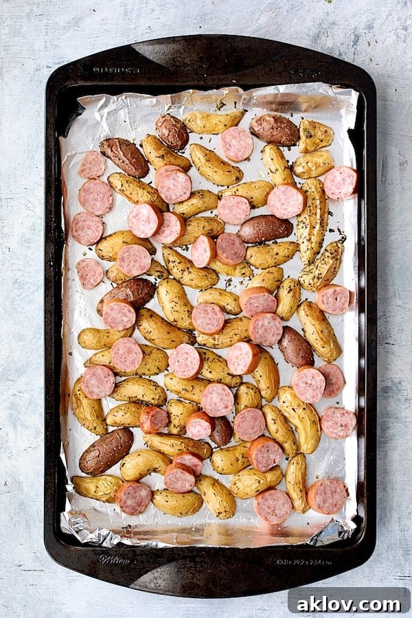 Semi-roasted fingerling potatoes mixed with sliced precooked sausage on a sheet pan, ready to continue roasting.