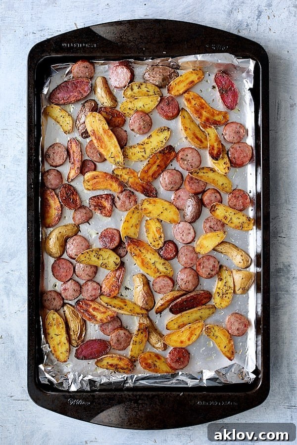 Fully roasted duck fat fingerling potatoes and perfectly cooked sausage slices, golden brown and glistening on a sheet pan.