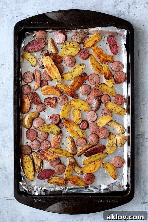 A close-up view of perfectly roasted potatoes and browned sausage on a sheet pan, glistening and ready to be served.