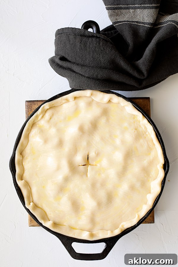 Unbaked chicken pot pie in a cast iron skillet, topped with a raw pastry crust, ready for the oven, showcasing the crimped edges and smooth surface.