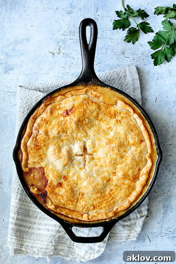 A freshly baked, bubbling Cheesy Skillet Chicken Pot Pie, golden-brown and steaming, presented on a blue towel, inviting hungry eyes.