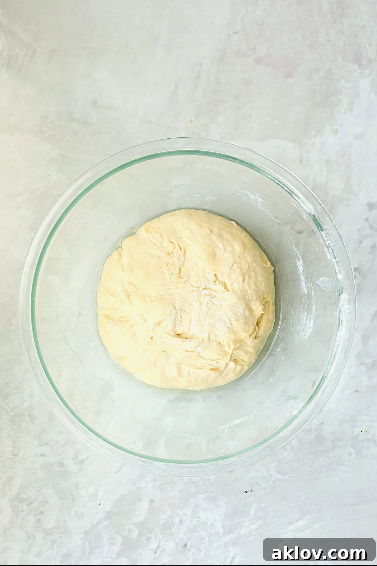 Pizza dough in a glass bowl, visibly risen and relaxed after its 10-minute rest.